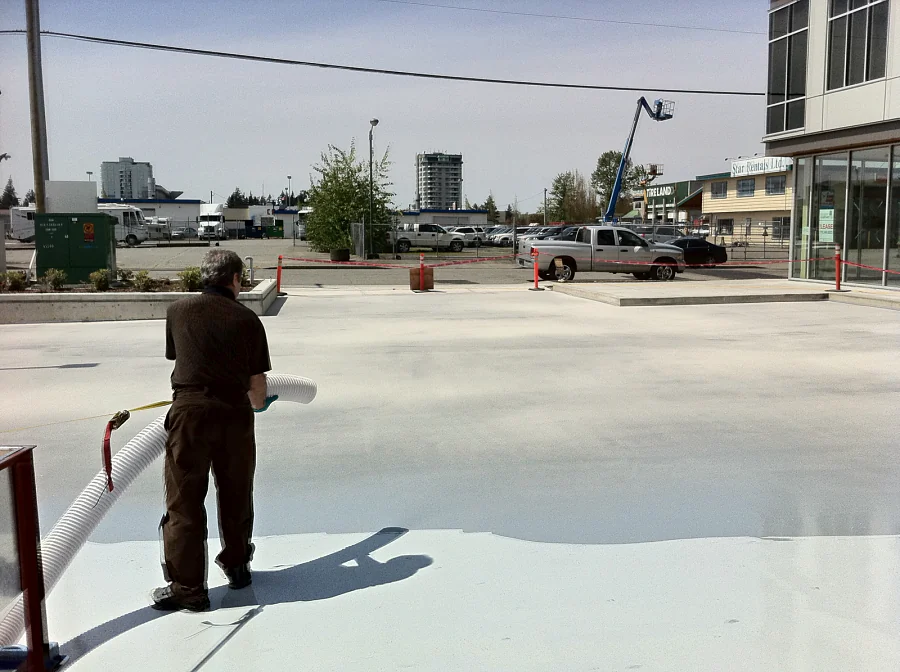 A crew member blowing aggregate by hose into the wet traffic coating on an exterior parkade deck in Abbotsford