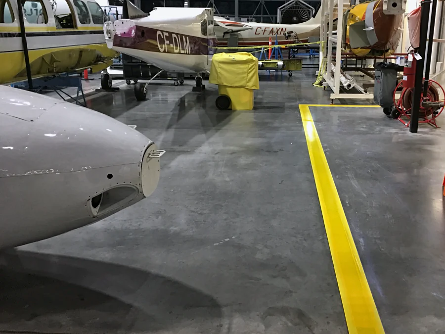 The same yellow urethane bay line finished on the hangar floor at the BCIT Aerospace Technology Campus, beside the nose of a training aircraft