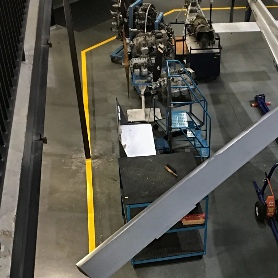 A yellow urethane walkway line round a bay of aircraft engines on their stands and a training helicopter, BCIT Aerospace Technology Campus, Richmond