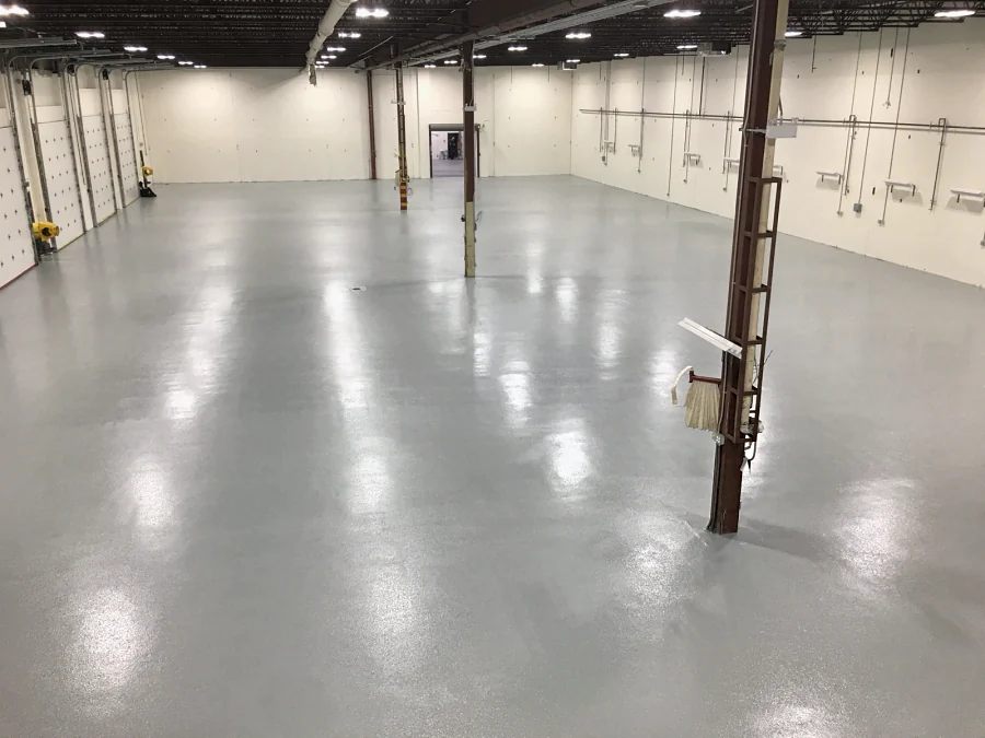 The finished epoxy and urethane floor, glossy light grey, down the warehouse past the overhead doors