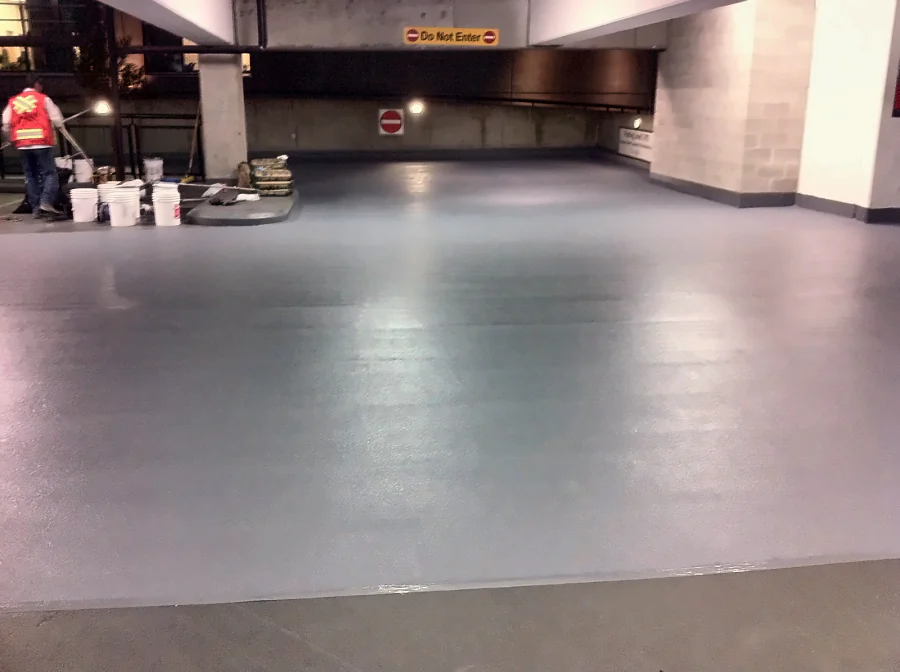 Grey textured traffic coating across a parking level of the Central City Shopping Centre parkade in Surrey, the crew and materials beyond