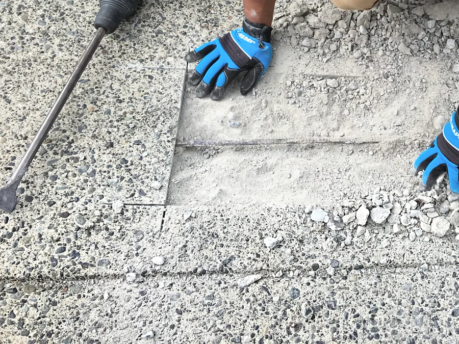 Loose concrete broken out with a hammer inside a saw-cut repair edge on a parkade entrance ramp
