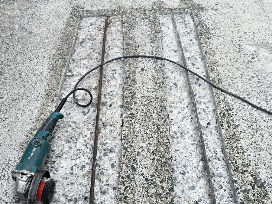 Two saw-cut repairs on the entrance ramp broken out to the rebar, the wire-brush grinder beside them