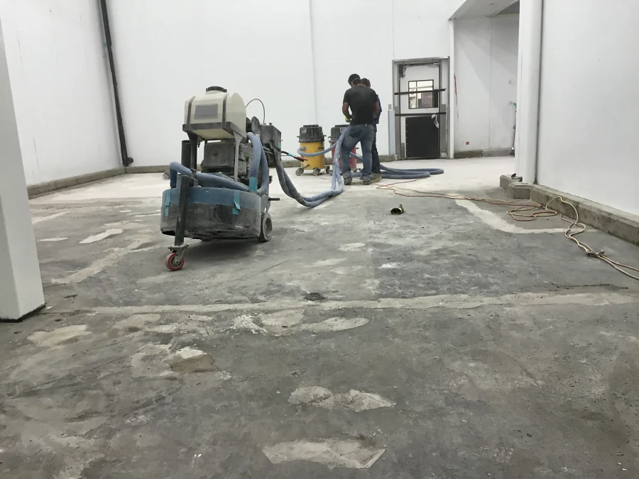 The concrete slab being ground under dust extraction before the decorative quartz floor at Costco Prince George, the patched areas showing pale