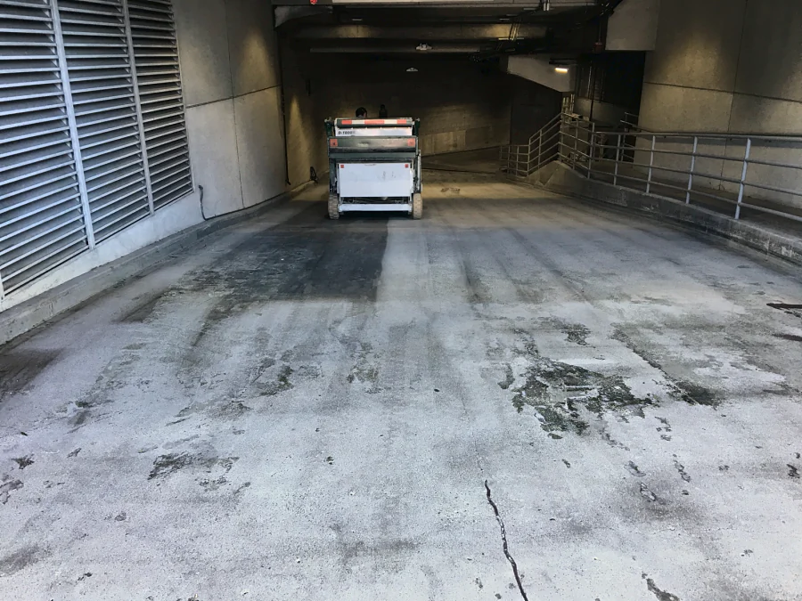 The entrance ramp of a commercial building parkade in Downtown Vancouver during surface preparation, a cracked and stained slab ahead of the machine