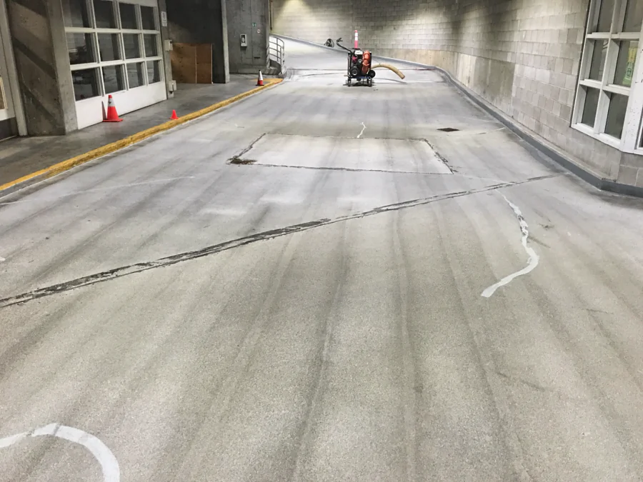 A parkade ramp in a Downtown Vancouver commercial building prepared for a traffic coating, its cracks and a patched section showing on the bare concrete