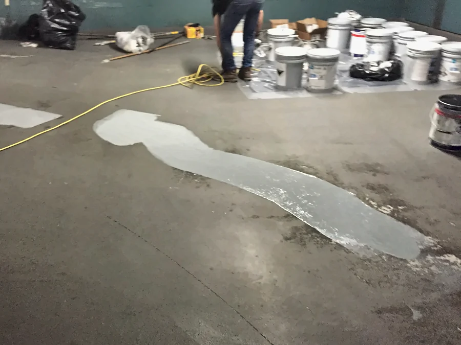 Repaired areas of a Downtown Vancouver parkade slab given their own grey coat before the full traffic coating, the materials staged on plastic behind