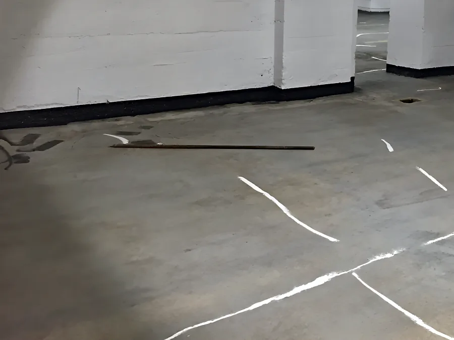 Cracks marked out in white across the parkade slab in Downtown Vancouver before repair and coating, the wall bases already black