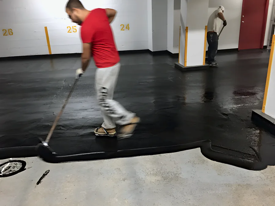 Crew spreading the black traffic coating by squeegee across a Downtown Vancouver parkade, the prepared concrete still bare in front