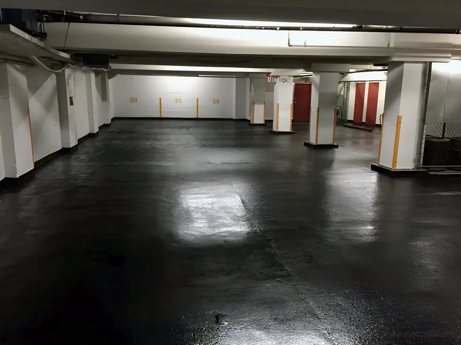 Black traffic coating across an underground parkade in Downtown Vancouver, against white walls, yellow stall numbers and column guards