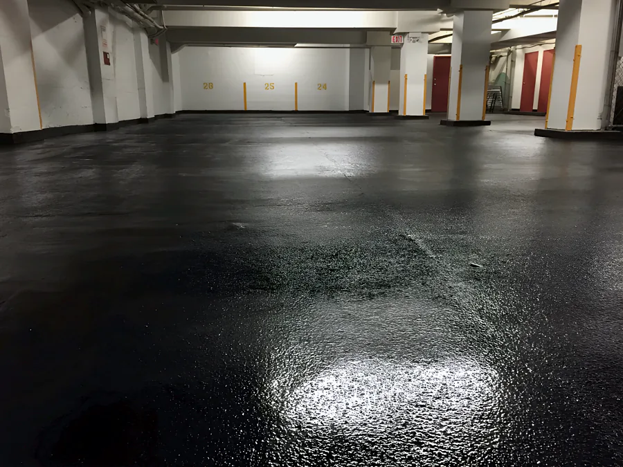Low view across the textured black traffic coating in a Downtown Vancouver parkade, glossy under the lights