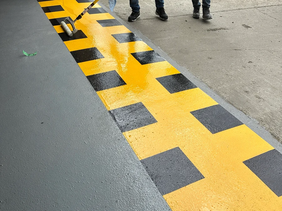 A yellow and black hazard stripe being rolled at the roller door threshold of a Finning workshop, on the new ResinTech EWS floor