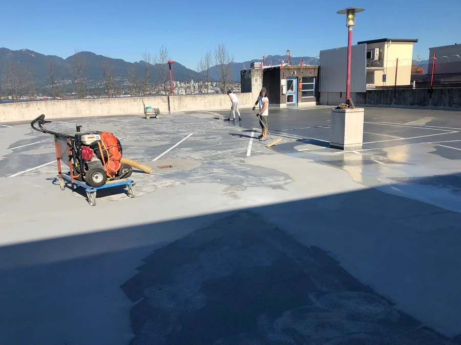 The crew sweeping the prepared parkade roof deck in Gastown, Vancouver, ahead of the new traffic coating, the North Shore beyond the parapet