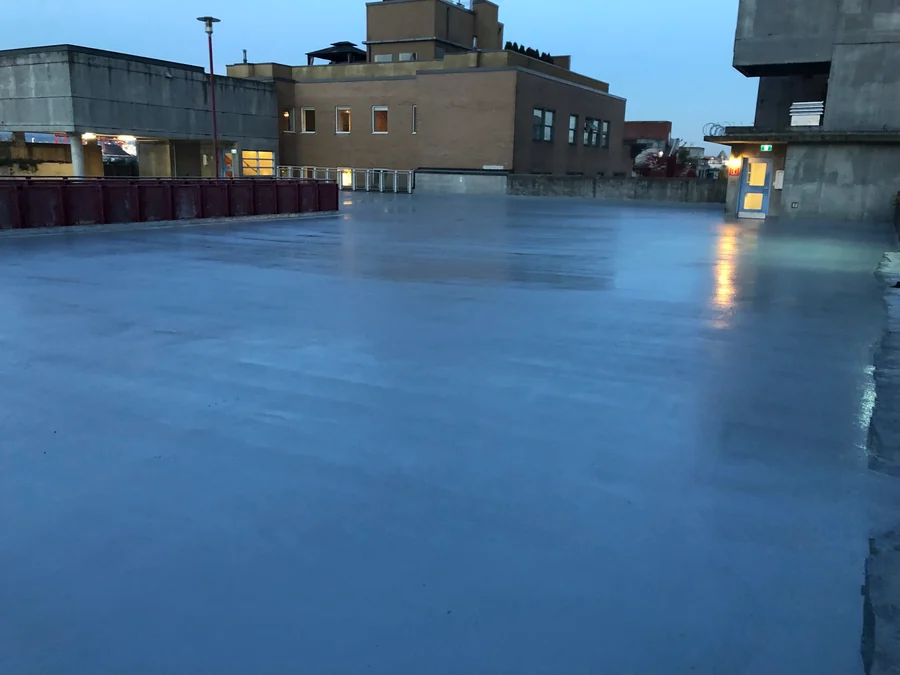 The recoated Gastown parkade roof deck at dusk, a door light reflected in the new traffic coating, Vancouver