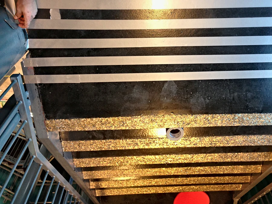 A black stair landing at Hard Rock Casino Coquitlam masked with tape for the warning strips, the gold flake stair nosings already laid below