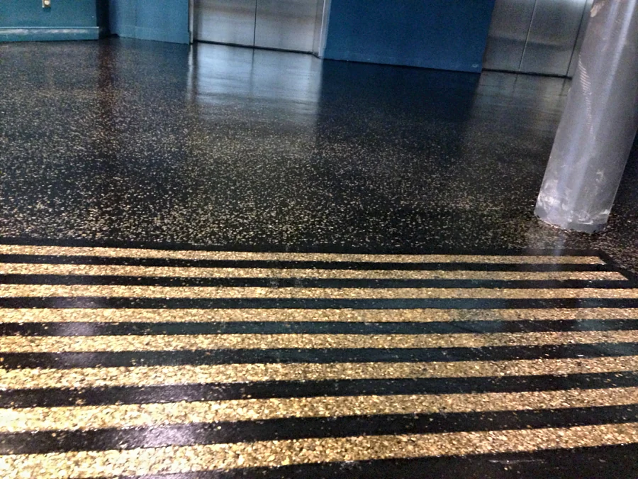 Black floor with a gold random flake broadcast by the elevators at Hard Rock Casino Coquitlam, a band of gold warning strips in front
