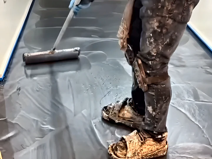 Installer spreading a metallic epoxy pour with a squeegee, wearing spiked shoes