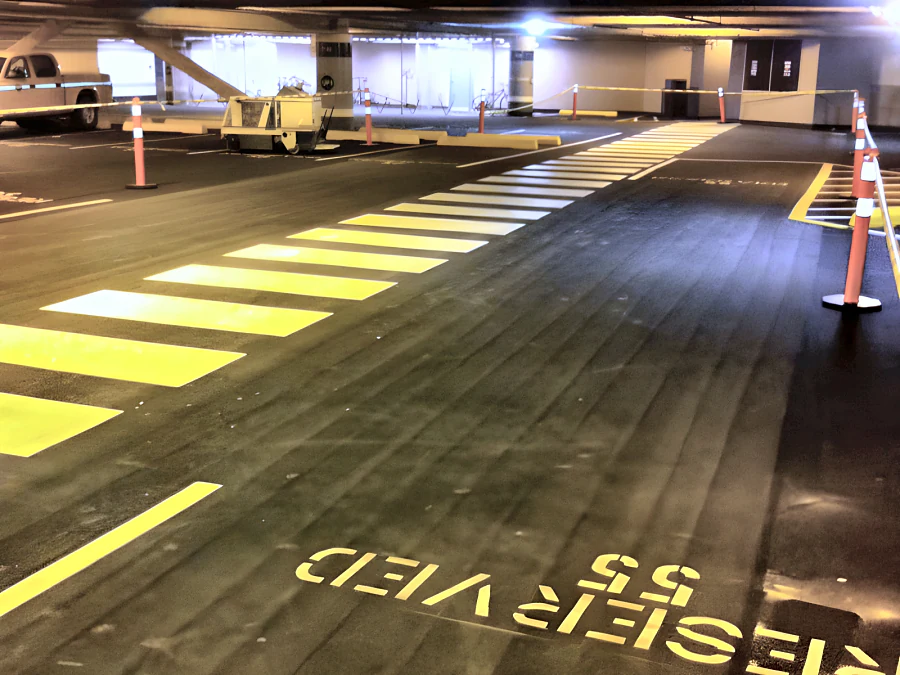 Dark parkade coating at Metrotown with new yellow crosswalk, stall lines and a reserved-stall marking