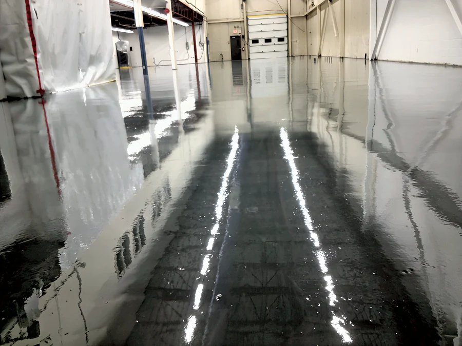 Fresh high-gloss grey floor coating in Building 2 at MTU Maintenance Canada, Richmond, with plastic containment still up along the side