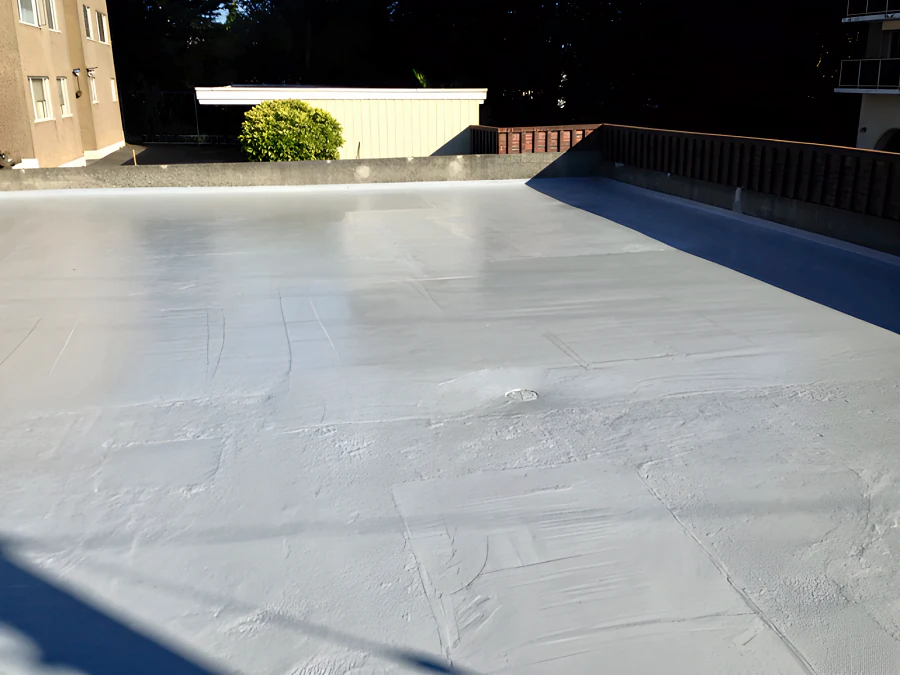 The membrane coat across the exterior parkade deck in New Westminster in evening sun, with the drain and the parapet upstand coated