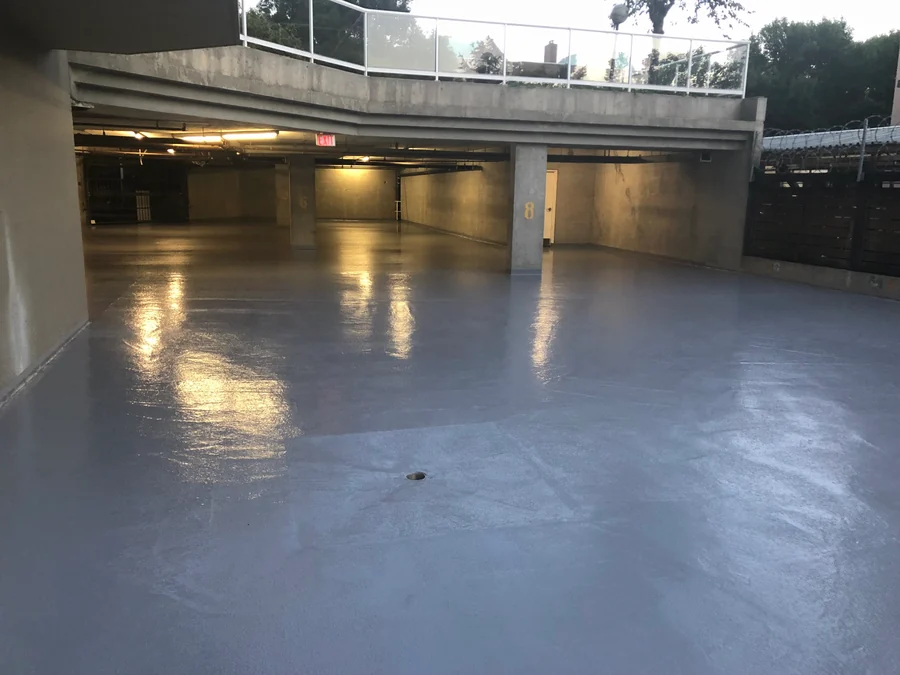 The finished Tremco Vulkem traffic coating across a residential tower’s parkade level in New Westminster at dusk, the coat past the drain to the open end