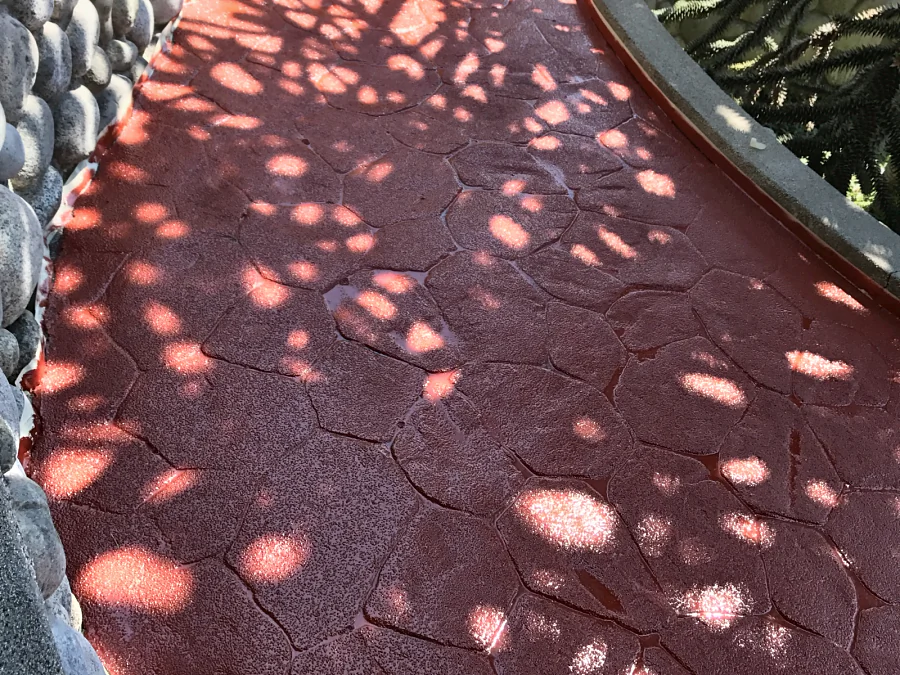 A garden path between river-stone walls in red ResinTech CRU anti-slip coating, the stamped flagstone pattern showing through