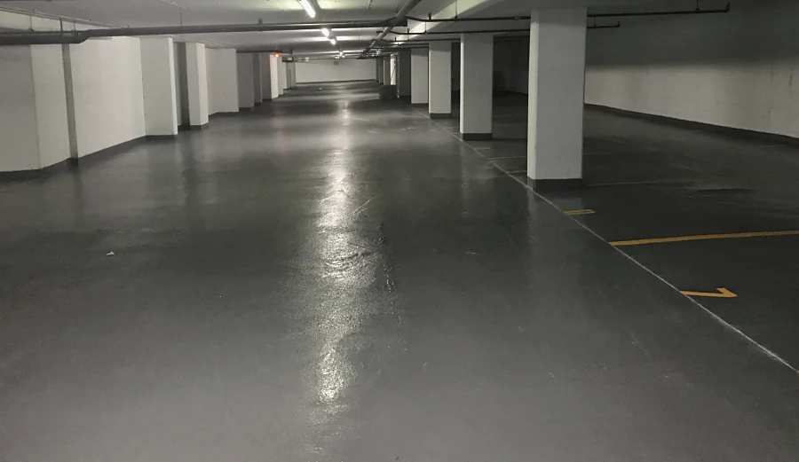A grey textured traffic coating down the drive aisle of an underground parkade, past the columns, the stalls lined in yellow, 2017