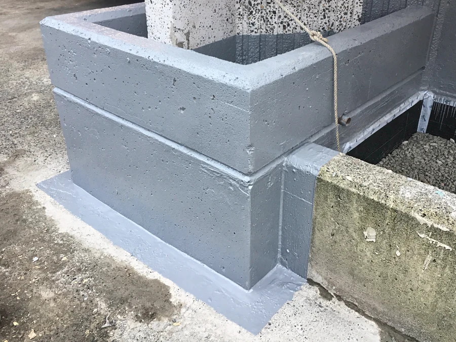 The corner of a planter waterproofed in ResinTech FPU and PPM, the grey membrane carried out onto the slab and turned up the exposed-aggregate column above it