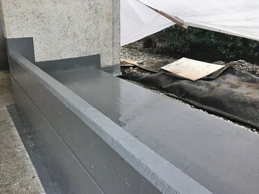 The top of the same planter coated in the grey ResinTech membrane, still glossy, turned up the building wall in a stepped detail