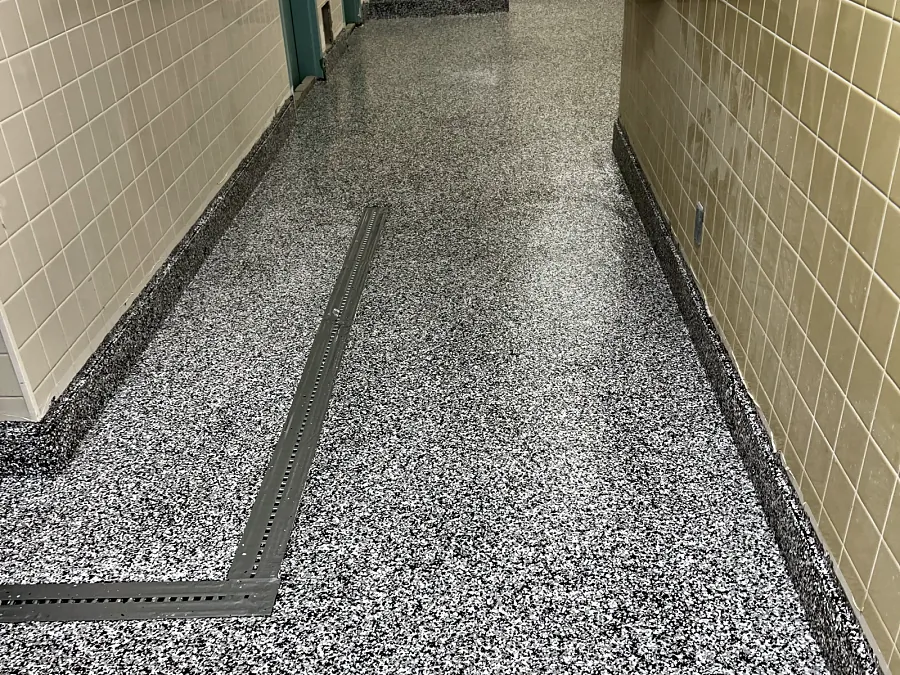 A ResinTech EWS flake floor along a tiled corridor, laid up to the trench drain, with a coved flake base on both walls