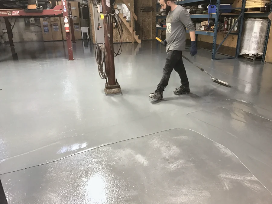 A light grey floor coating being spread by squeegee round a steel column in a Richmond mechanic shop, 2017