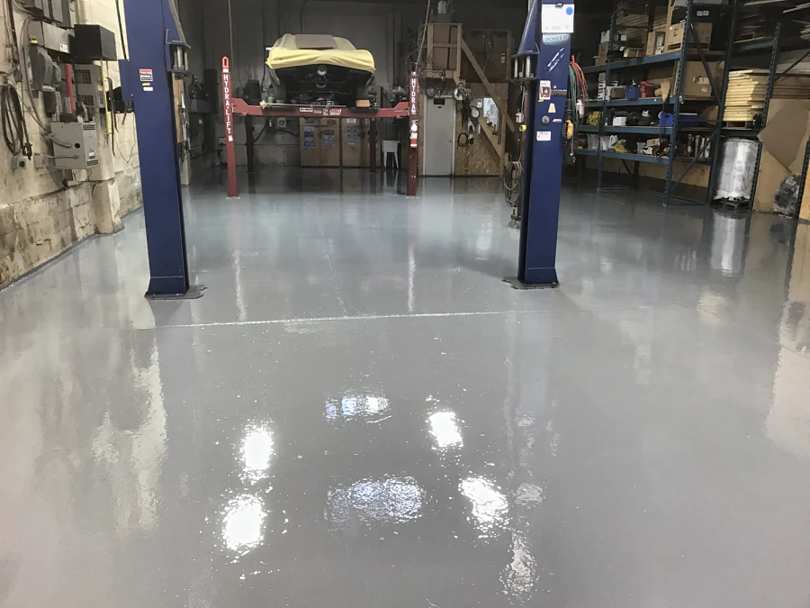 The finished light grey floor between the posts of a two-post hoist, the four-post hoist beyond, 2017