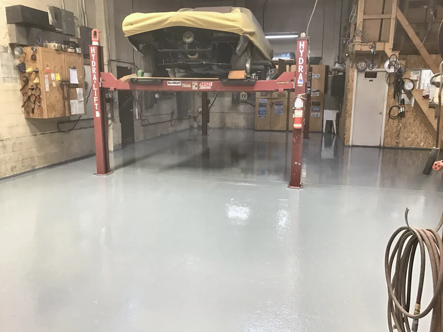 A light grey high-gloss floor coating under a four-post hoist in a Richmond mechanic shop, 2017
