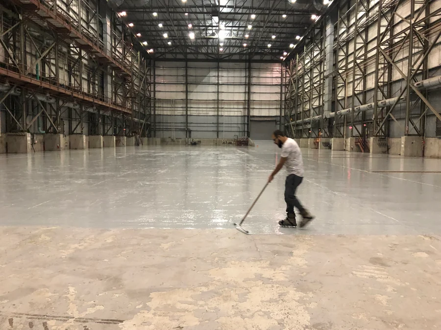 The epoxy being squeegeed across the slab of the hall, the bare concrete still ahead of the coat, Seaspan, North Vancouver, 2018
