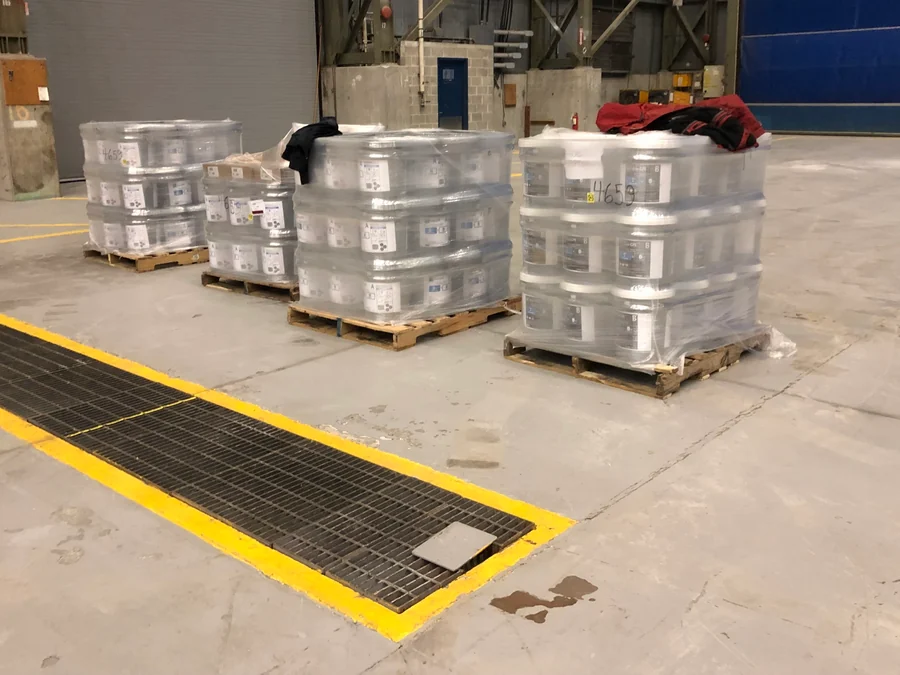 Pallets of epoxy staged on the slab beside a trench grate before the pour, Seaspan, North Vancouver, 2018