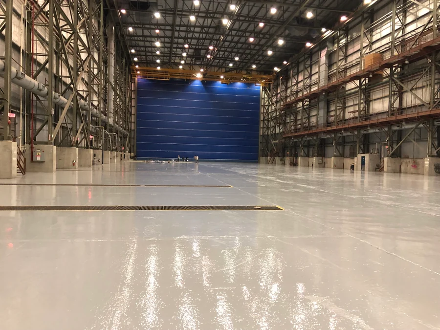 The finished grey epoxy floor running the length of a steel-framed hall to its full-height door, a 60,000 square foot job for Seaspan in North Vancouver, 2018