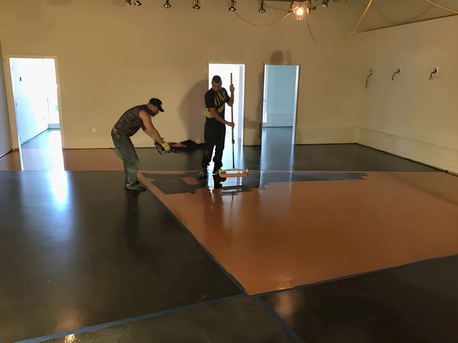 Crew rolling the orange urethane coat inside a taped-off diagonal section of a showroom floor