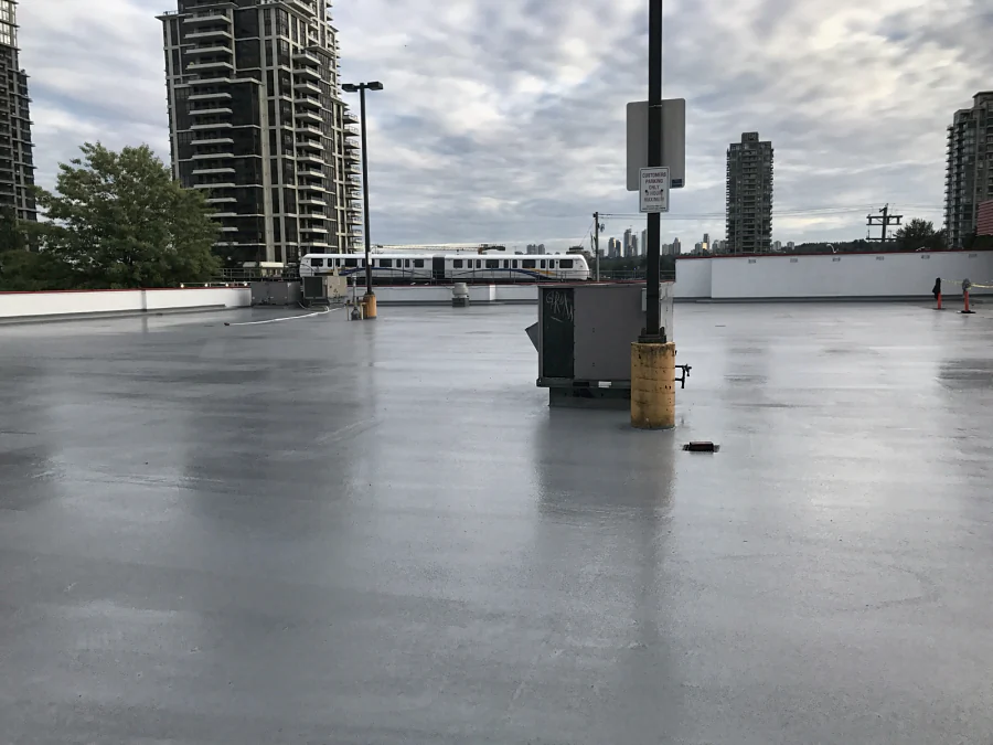 The finished rooftop parkade deck of a Staples store in Burnaby round a rooftop unit, the SkyTrain passing beyond the parapet