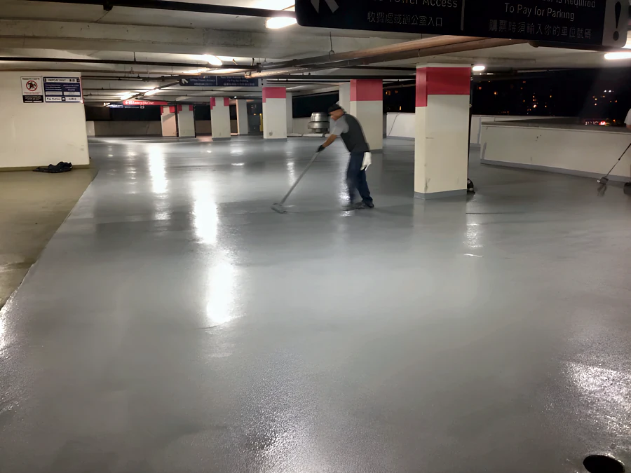 Crew rolling out the grey traffic coating through the Three West Centre parkade in Richmond after dark, past the red-banded columns