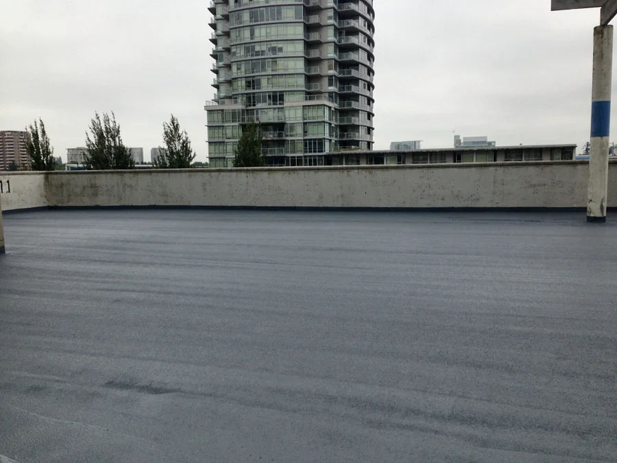 The open roof deck finished in a dark grey textured traffic coating, a residential tower beyond