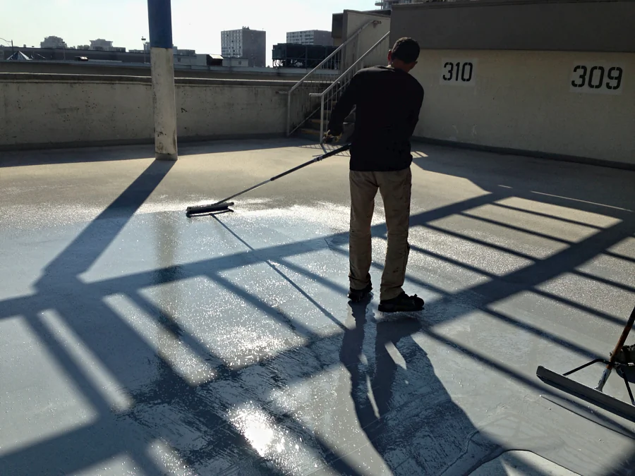 A crew member spreading the grey coat by squeegee across the roof deck of the Three West Centre parkade in Richmond, stalls 309 and 310 behind