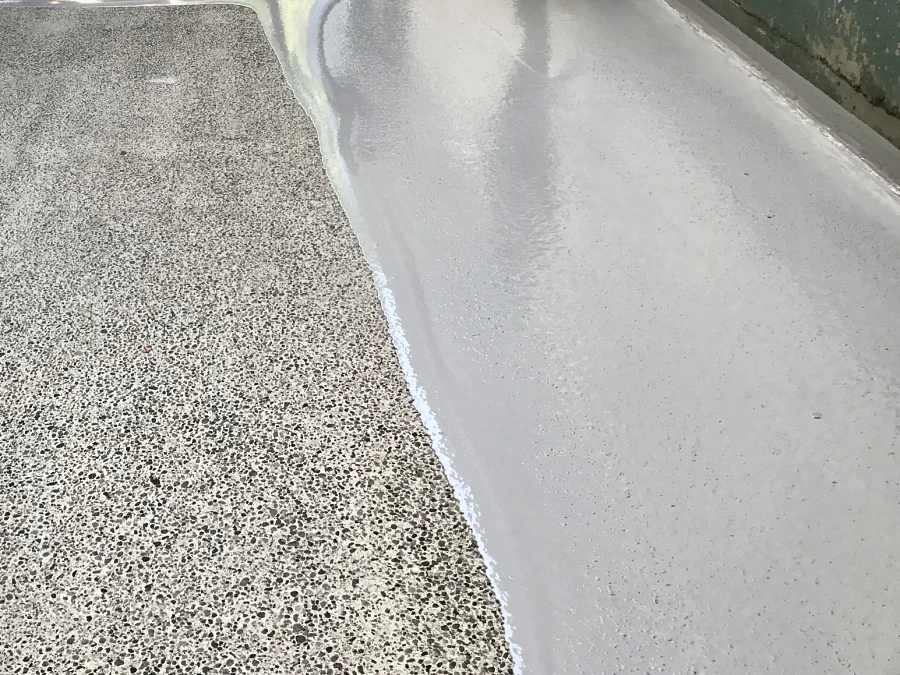 The edge of the new grey coat over the bare exposed-aggregate concrete at the foot of the Vancity parkade ramp in Vancouver