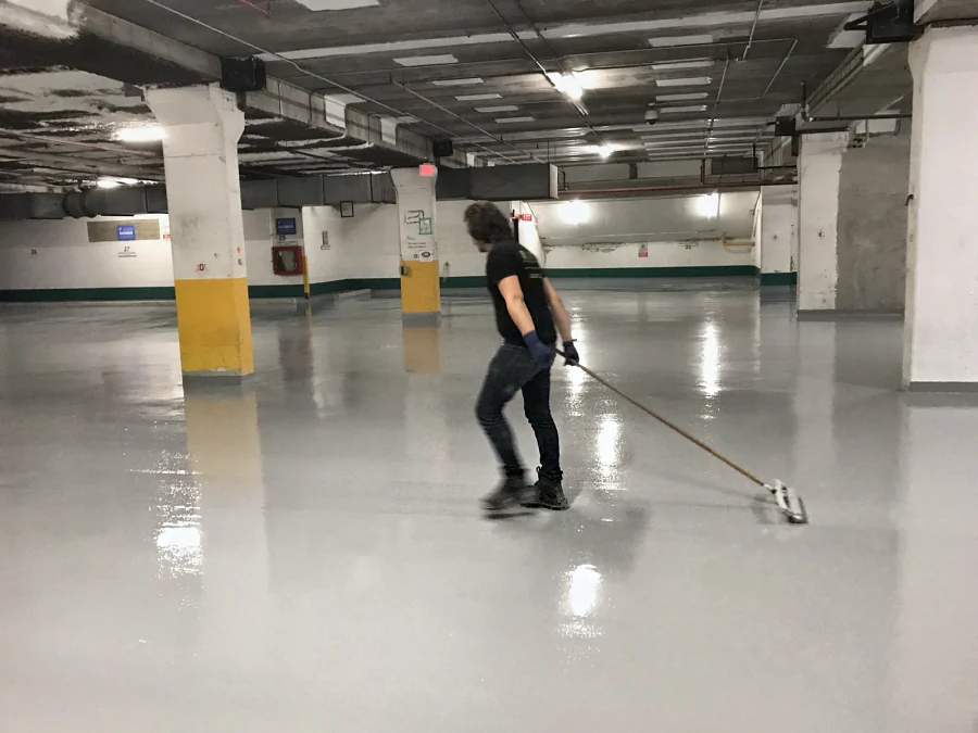 A crew member spreading the grey traffic coating by squeegee across a parking level of the Vancity parkade in Vancouver