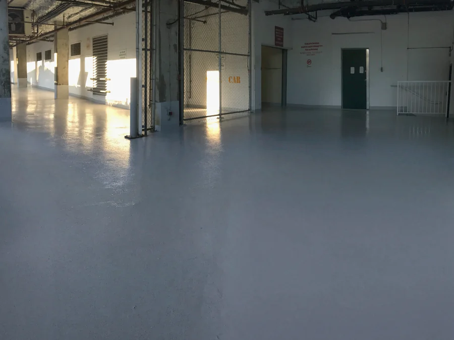 The finished loading bay in daylight, the grey Tremco Vulkem 350NF/346 coat running back to the garbage enclosure gate and the service door