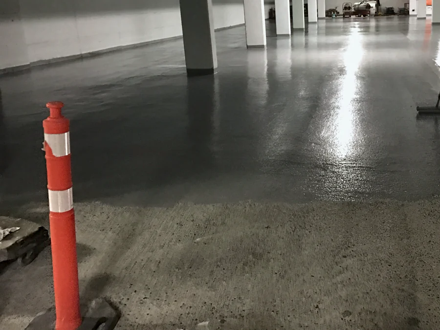 A Tremco Vulkem 350NF/950NF/950NF traffic coating squeegeed across a parking level of a Vancouver parkade, past the columns, the prepared slab still bare in front