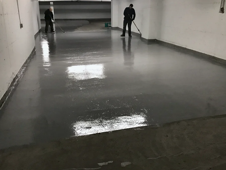 The crew spreading a grey Tremco Vulkem 350NF/950NF/950NF traffic coating by squeegee along a drive aisle of a 30,000 square foot Vancouver parkade for Lark Group