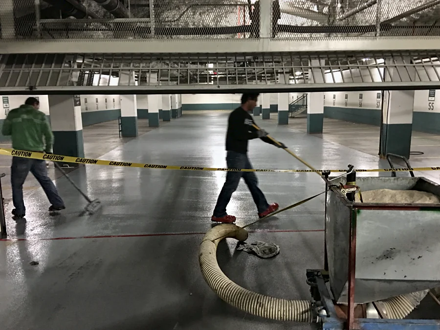 The crew working a parkade top coat in Vancouver, the hopper of aggregate beside the tape line, seen through the parkade gate