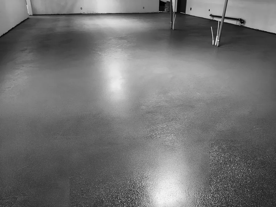 Finished epoxy and urethane warehouse floor with a textured, glossy surface, laid round the pipes and up to the walls