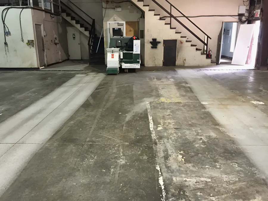 Shot-blasted lanes across the old warehouse slab, cleaned back to bare concrete through the stained and painted surface