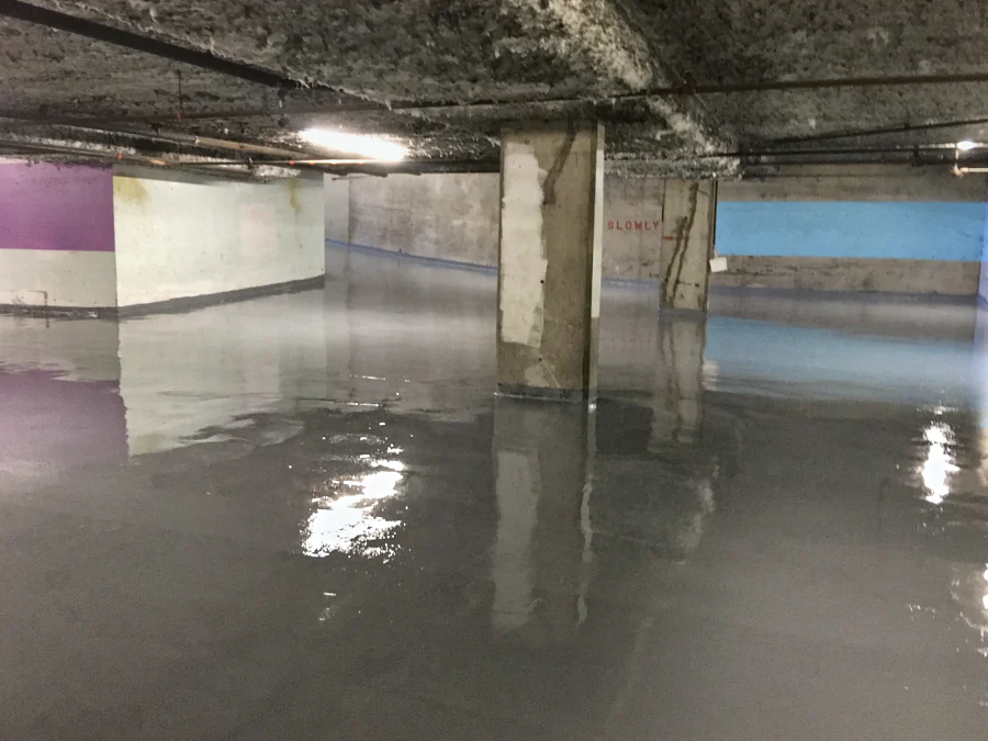 The grey Mapei traffic coating going down across a residential parkade on West Broadway, Vancouver, still wet round the columns